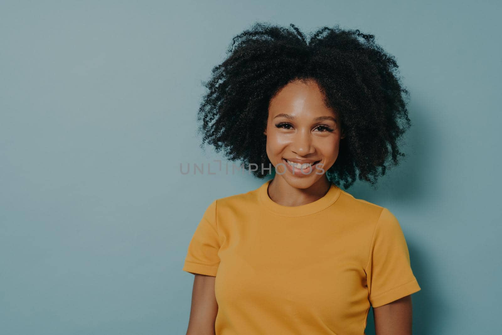 Happy dark skinned woman smiling at camera with pleased face expression, isolated on blue background by vkstock