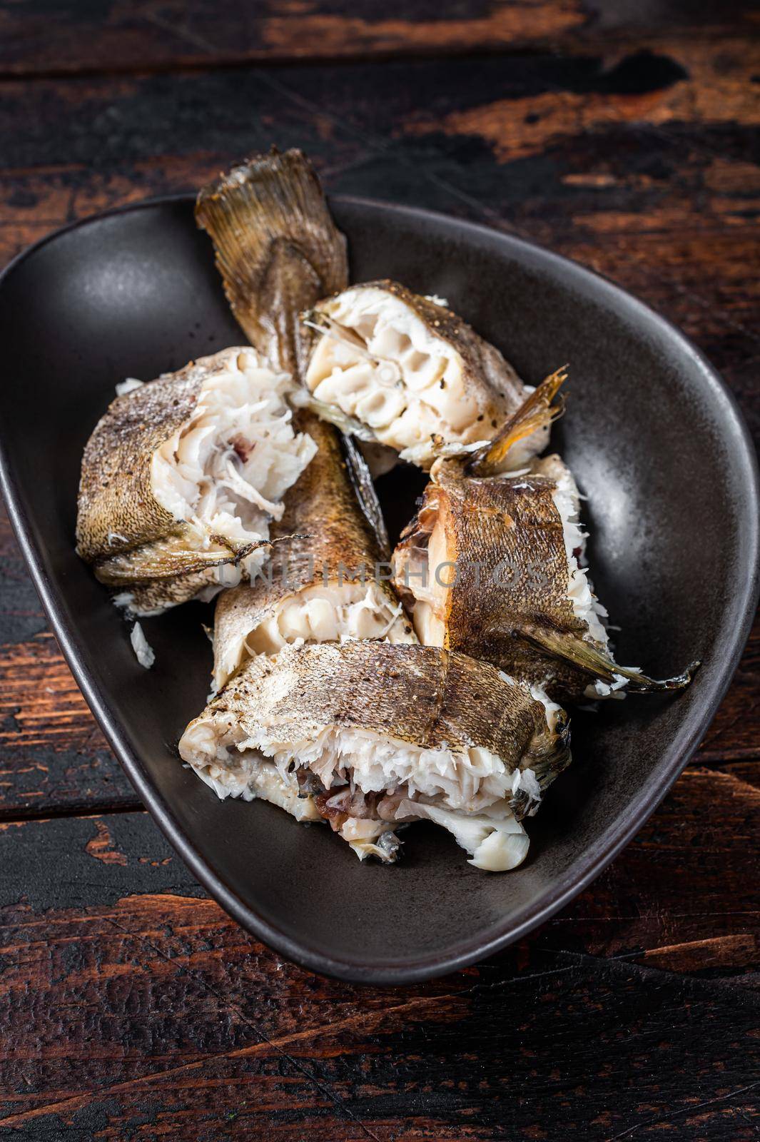 Roasted hake white fish in a plate. Dark wooden background. Top view.