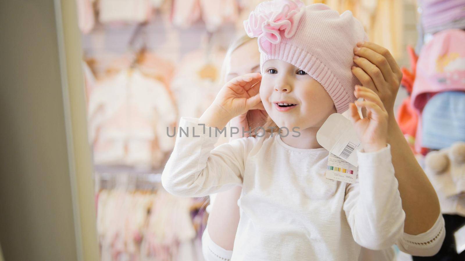 Portrait of happy blonde child girl doing shopping in kids dress store, telephoto