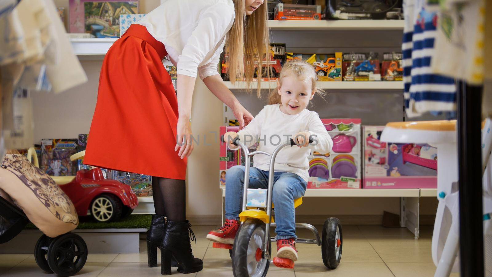 Happy little girl plays with kids bicycle in children's store, close up