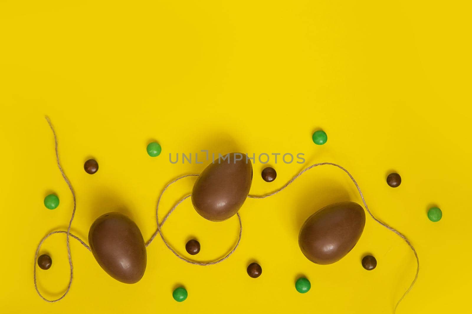 Flat lay composition with chocolate Easter eggs and chocolate sweets on yellow background. View from above, empty space for text. by Annu1tochka