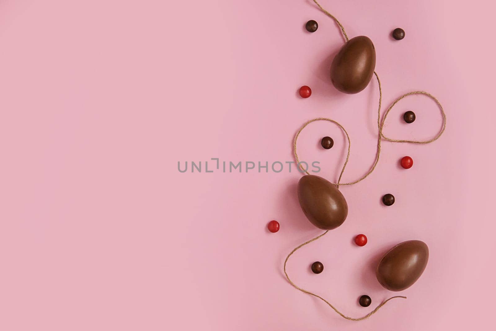 Flat lay composition with chocolate Easter eggs and chocolate sweets on pink background. View from above, empty space for text. by Annu1tochka