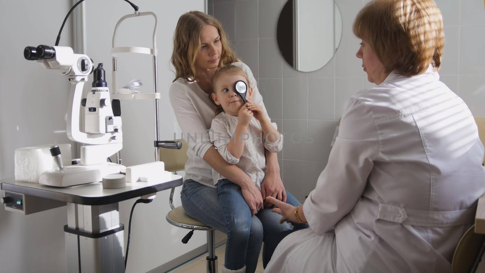 Ophthalmologist in clinic explains diagnosis about girl's eyesight - child plays, horizontal