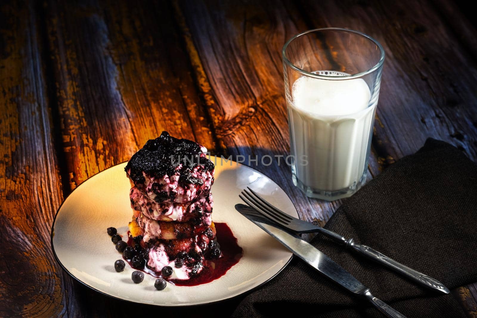 Cheesecakes with blueberry jam and sour cream on a plate with a glass of milk on the table by Lobachad