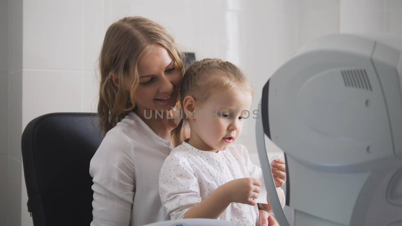Optometrist checks child's eyesight - mother and child in ophthalmologist room, horizontal