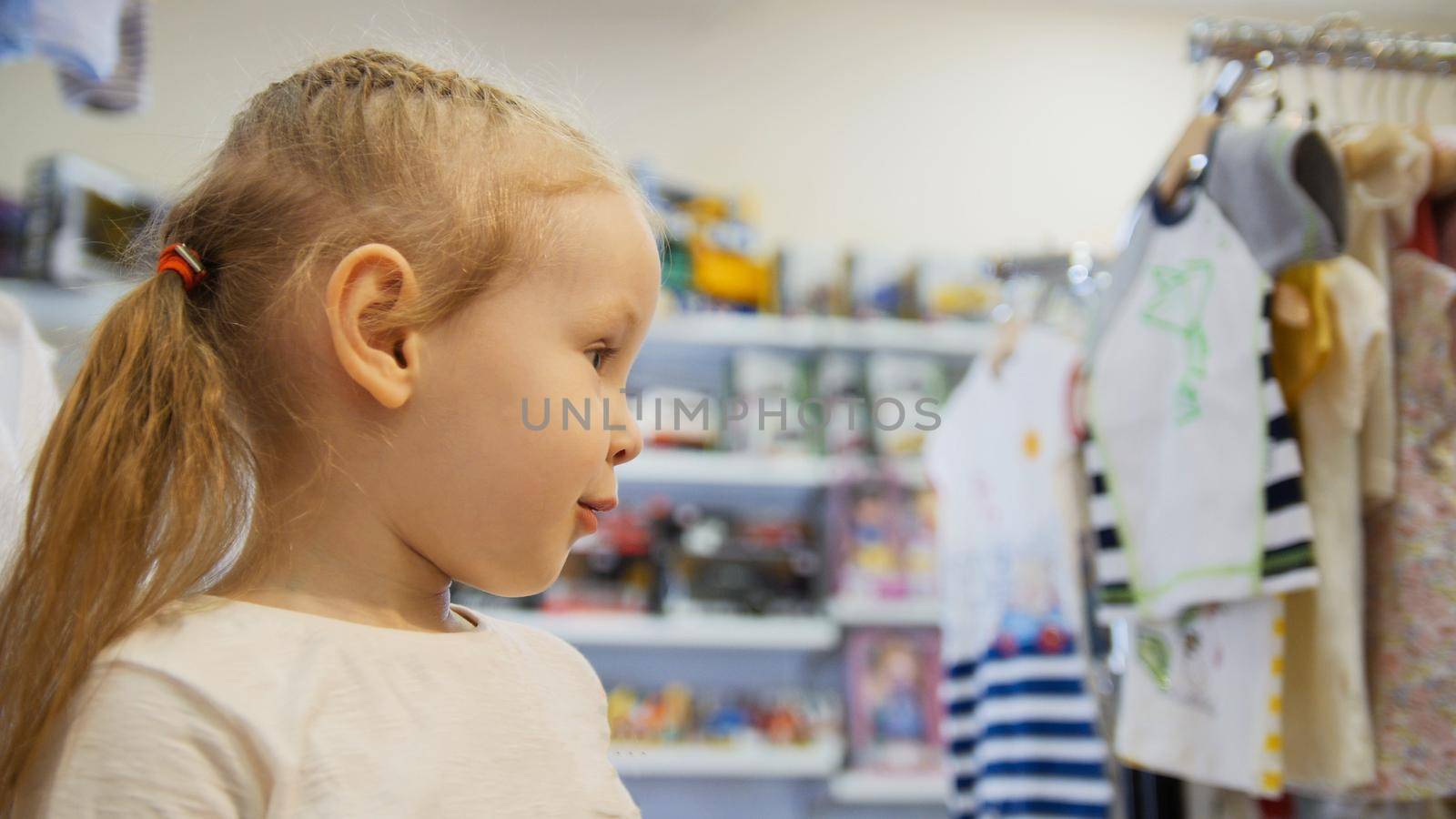 Cute blonde baby girl in child dress store, telephoto