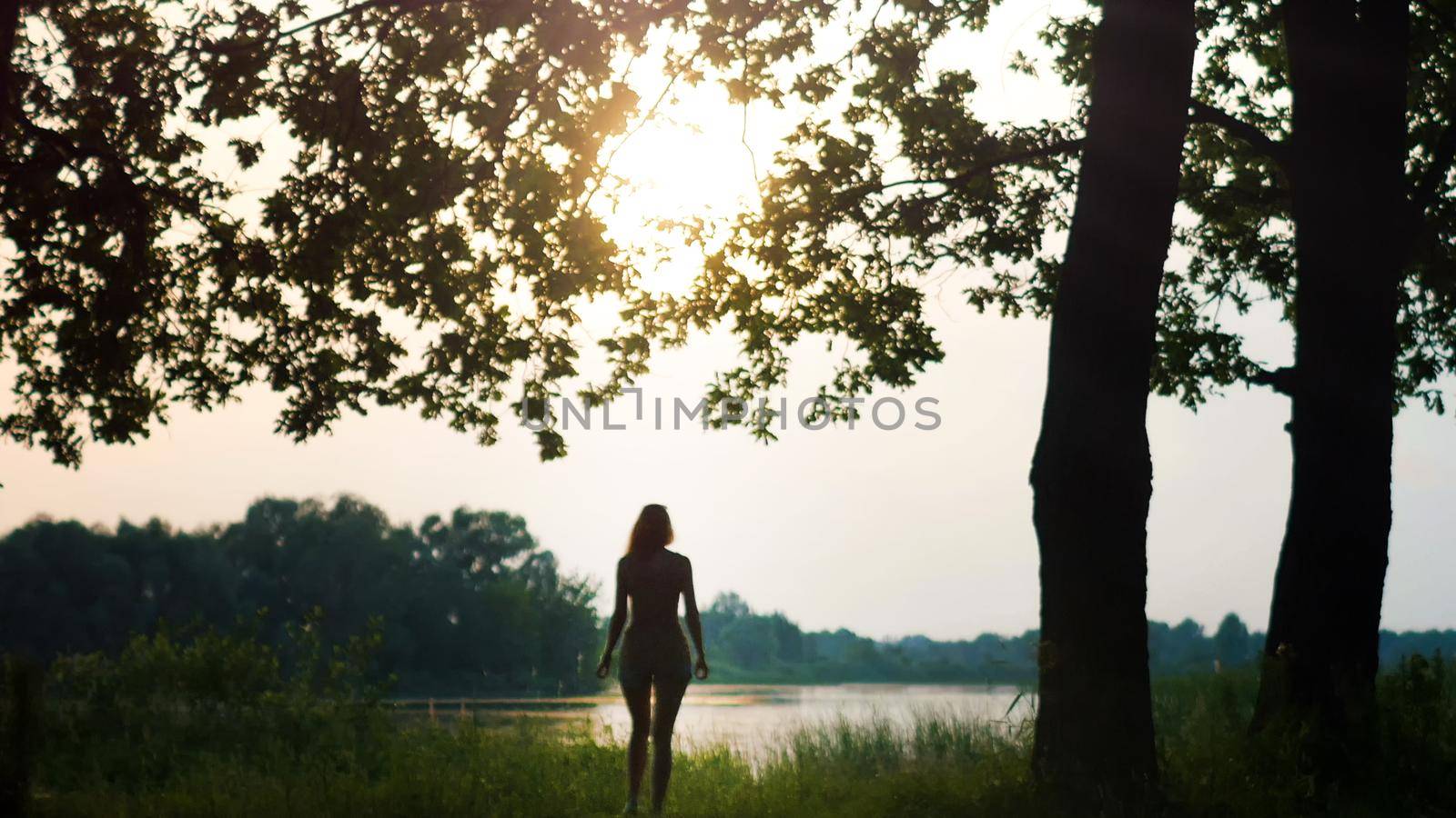 Beautiful Young Woman near forest lake at sunrise or dusk, silhouette, telephoto