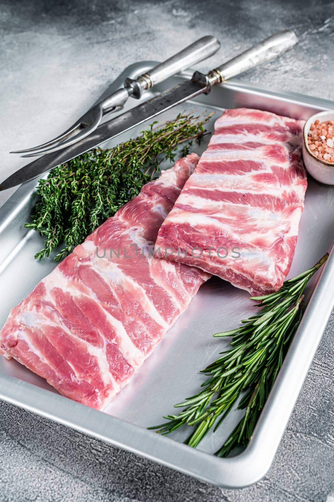 Rack of Raw pork spare ribs in kitchen oven tray with herbs. White background. Top view.