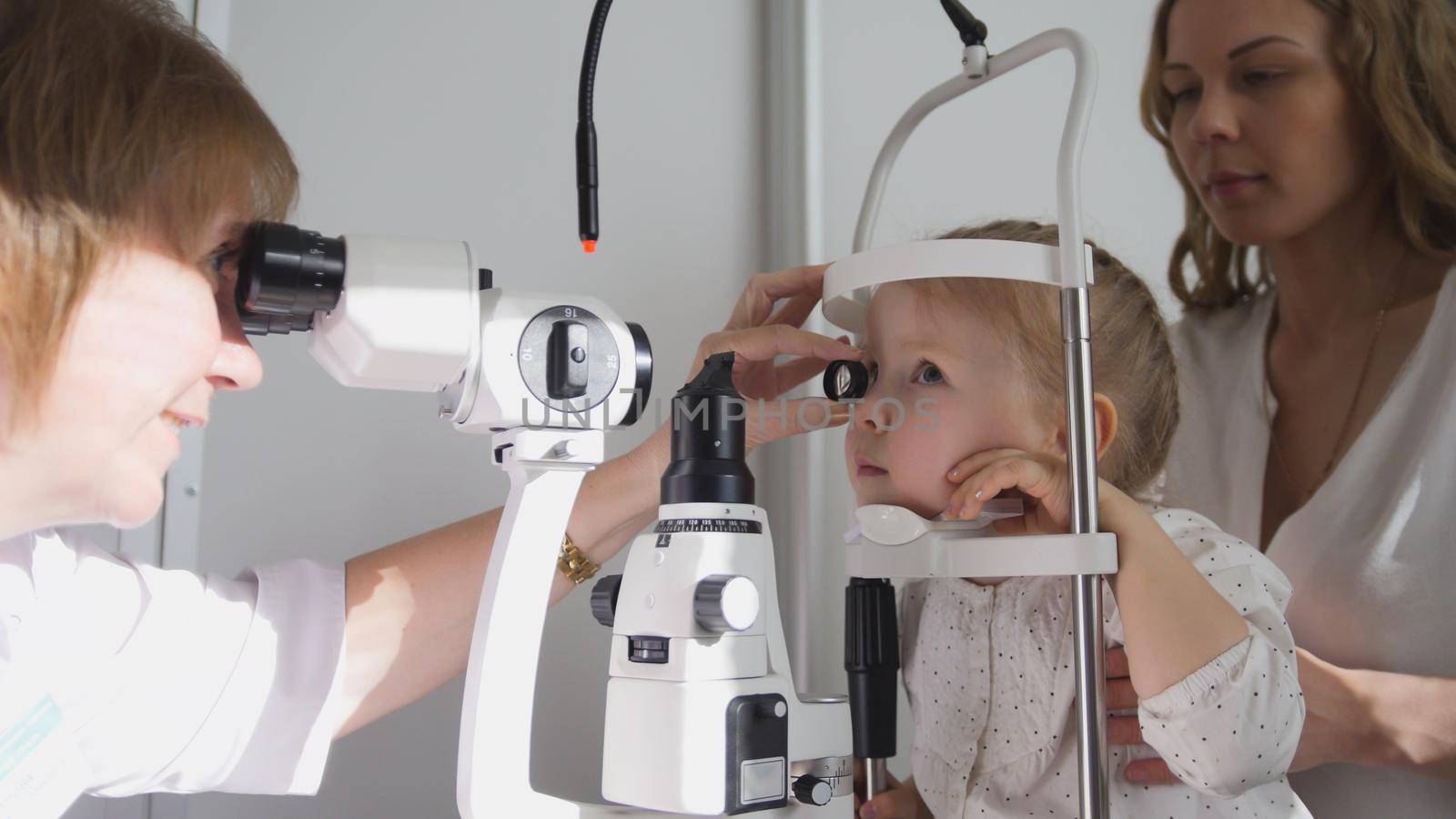 Optometrist checks little girl's eyesight - mother and child in ophthalmologist room, horizontal