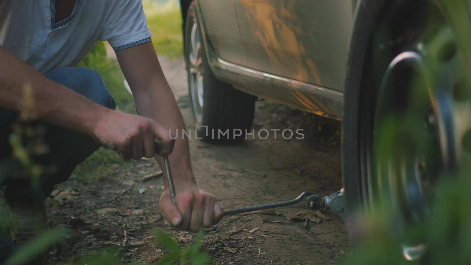 Close up view of man changes broken wheel of a car in the woods, telephoto