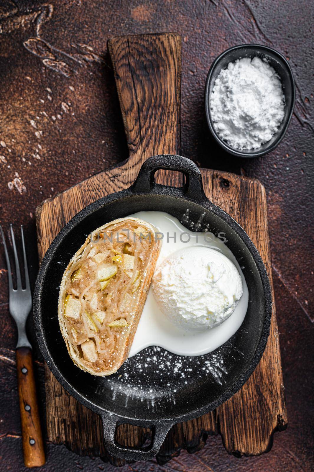 Apfelstrudel strudel with cinnamon, powdered sugar and vanilla ice cream in a pan. Dark background. Top view.