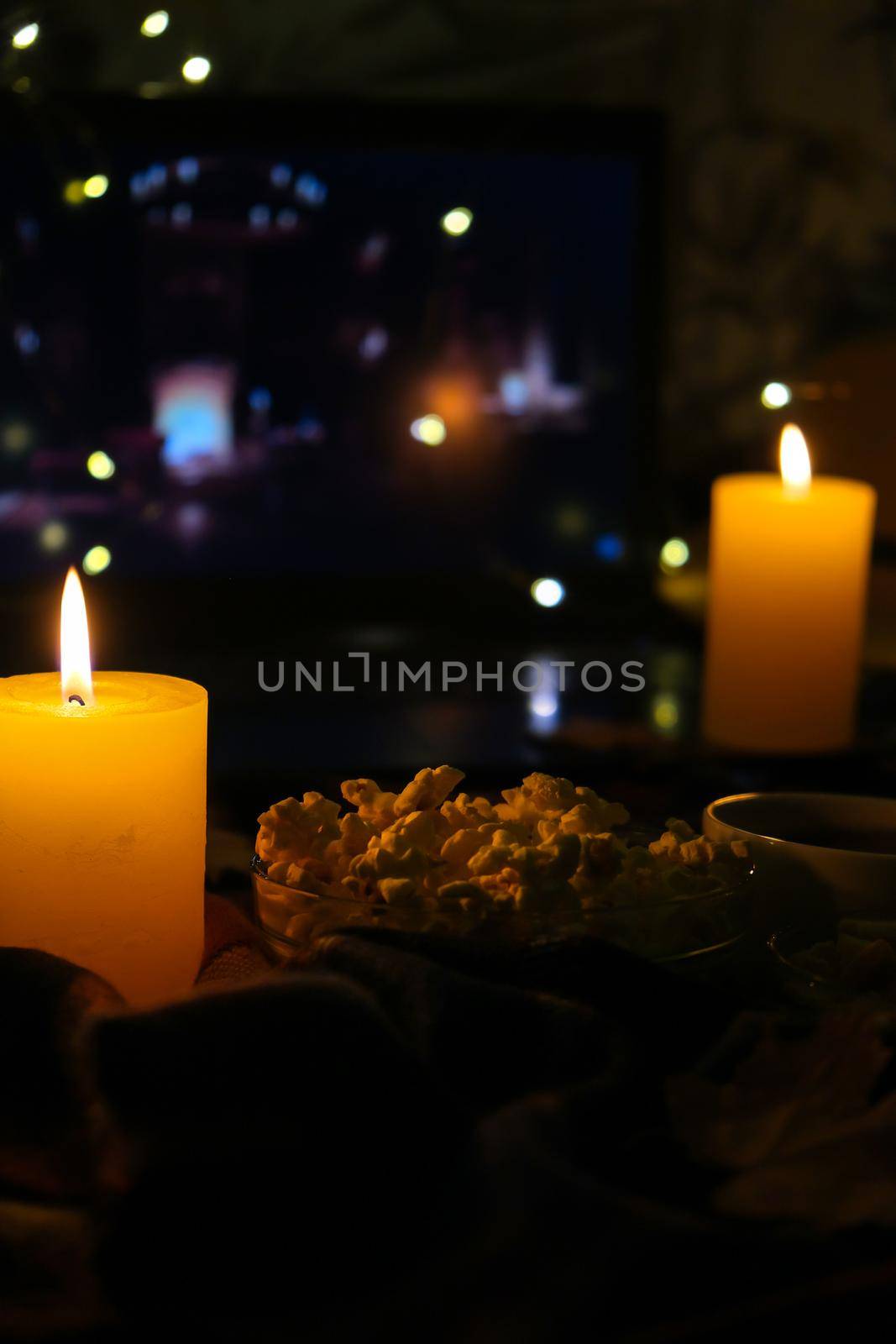 Movie on laptop at night in bedroom lit with candles. Pop corn. Autumn atmosphere at home by anna_stasiia