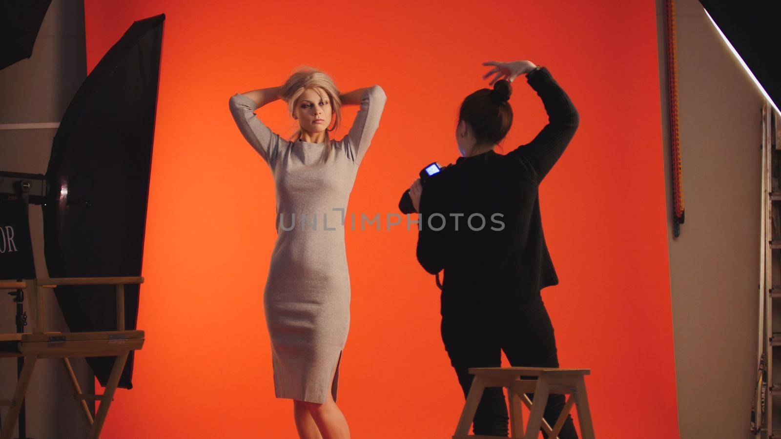 Adorable blonde girl posing for photographer - fashion backstage, red background