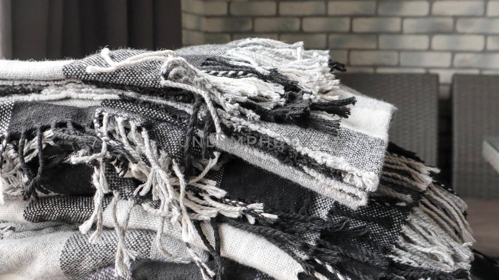 heap of knitted plaids on a gray background. Warm and cozy woolen decor for home and cafe. Gray wall background. Copy space. Gray checkered blanket. Warm and cozy home, selected focus.