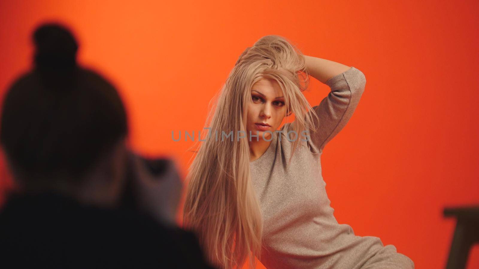 Backstage: blonde female model posing for photographer in red studio, close up
