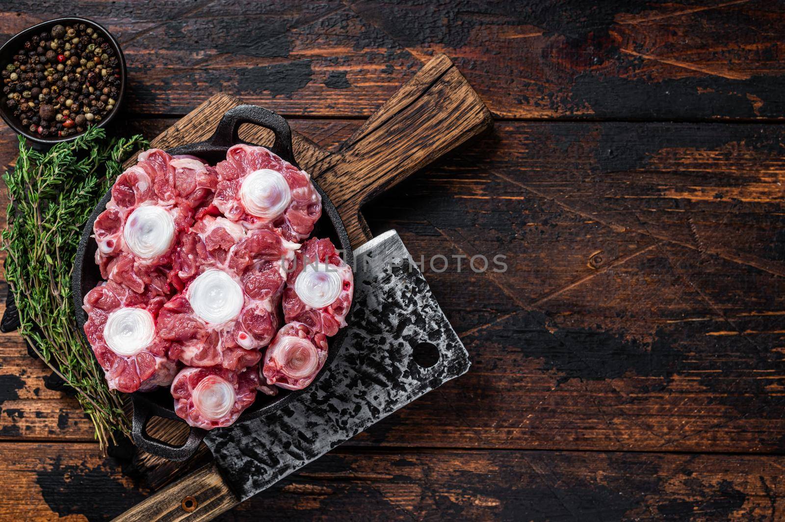 Raw veal beef Oxtail Meat on butcher wooden board with cleaver. Dark wooden background. Top view. Copy space by Composter