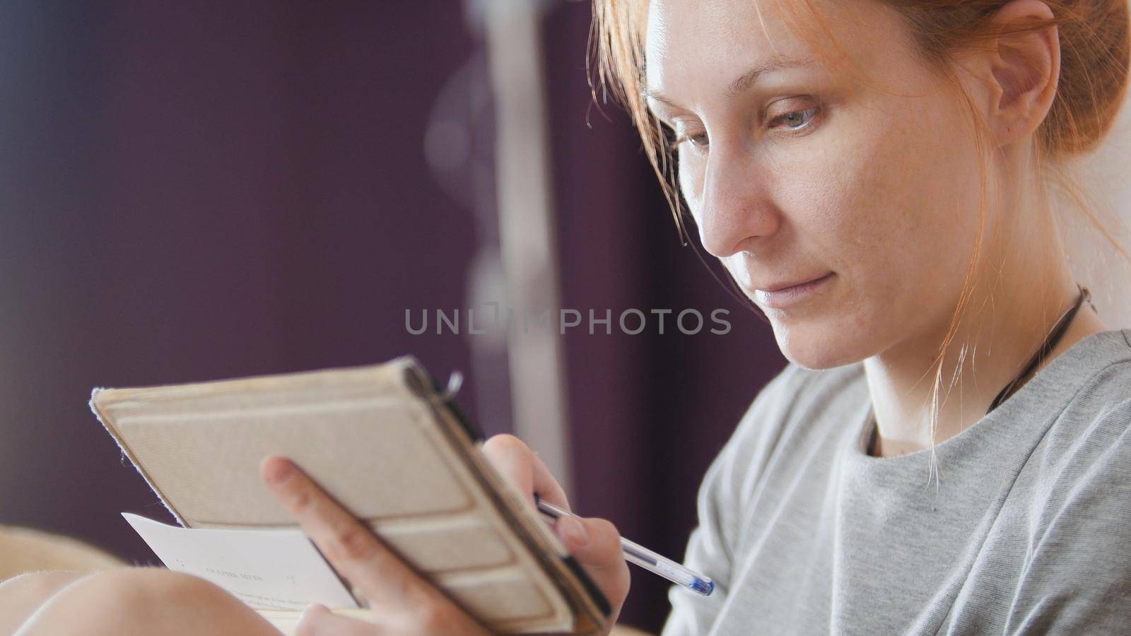 Portrait of a pretty woman at home sitting at sofa and working with gadget and notebook, close up