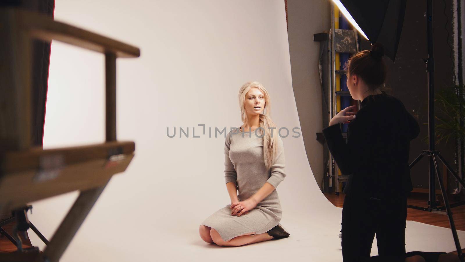 Fashion photo backstage - Blonde handsome girl posing for photographer - model sits at knees, white background