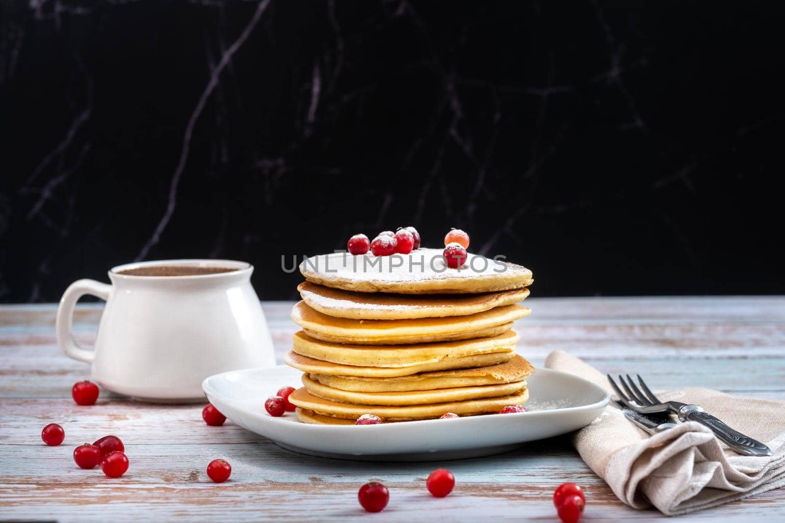 morning breakfast of pancakes with cranberries and powdered sugar and a cup of coffee on a wooden table.