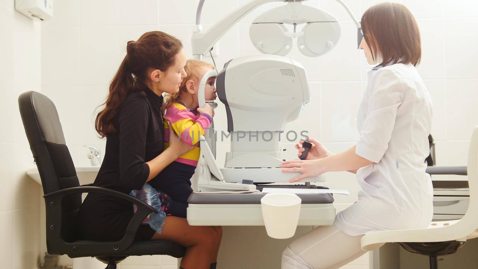 Mother with child in eye clinic - children ophthalmology - optometrist Checks Child's Eye, horizontal