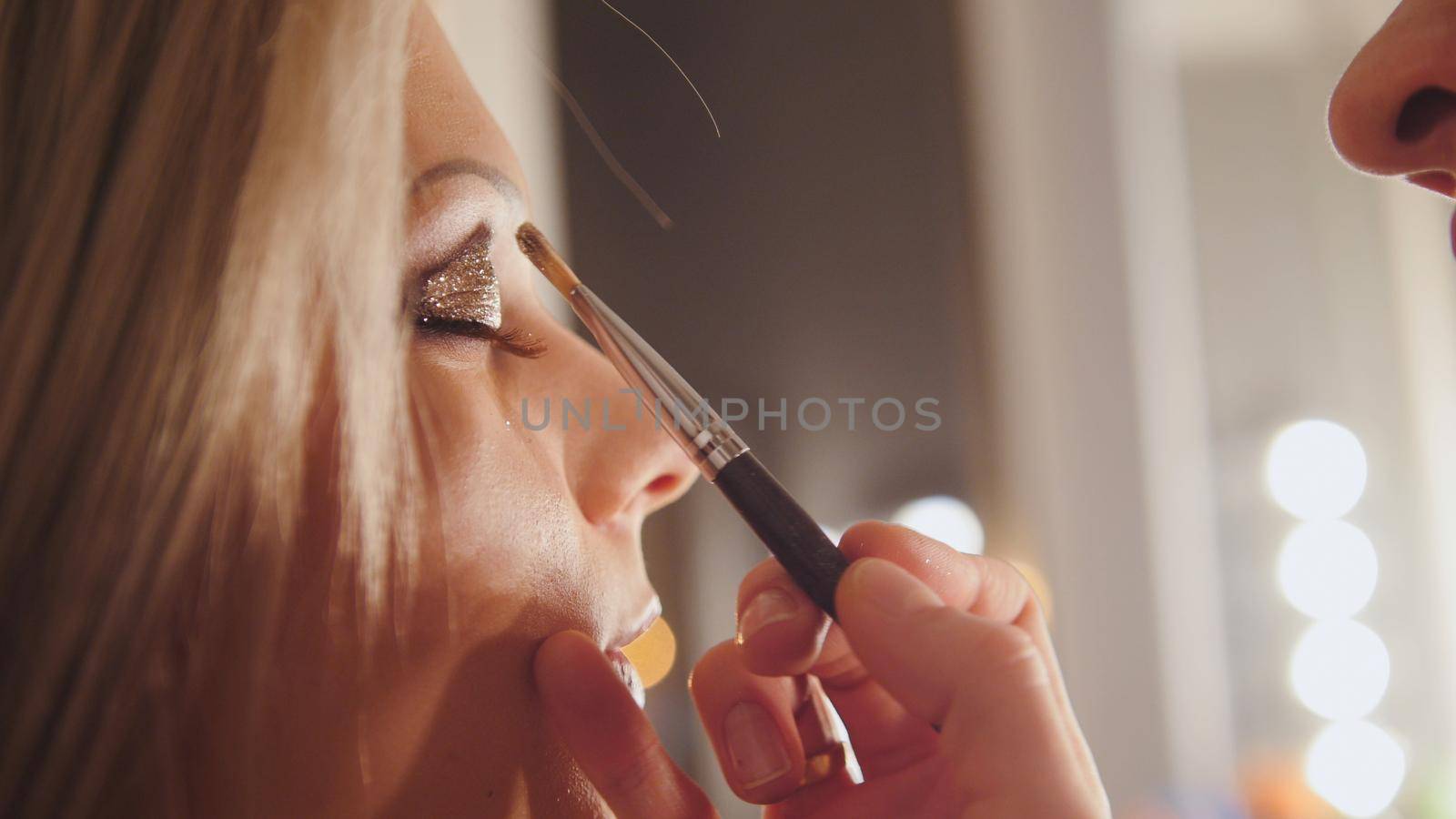 Beauty shop: makeup artist creates makeup for eyebrows of attractive young woman, telephoto, close up