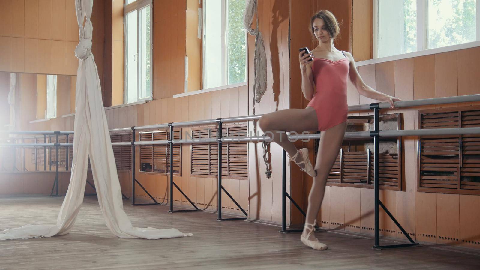 Young woman dancer use smartphone in a ballet room, wide angle