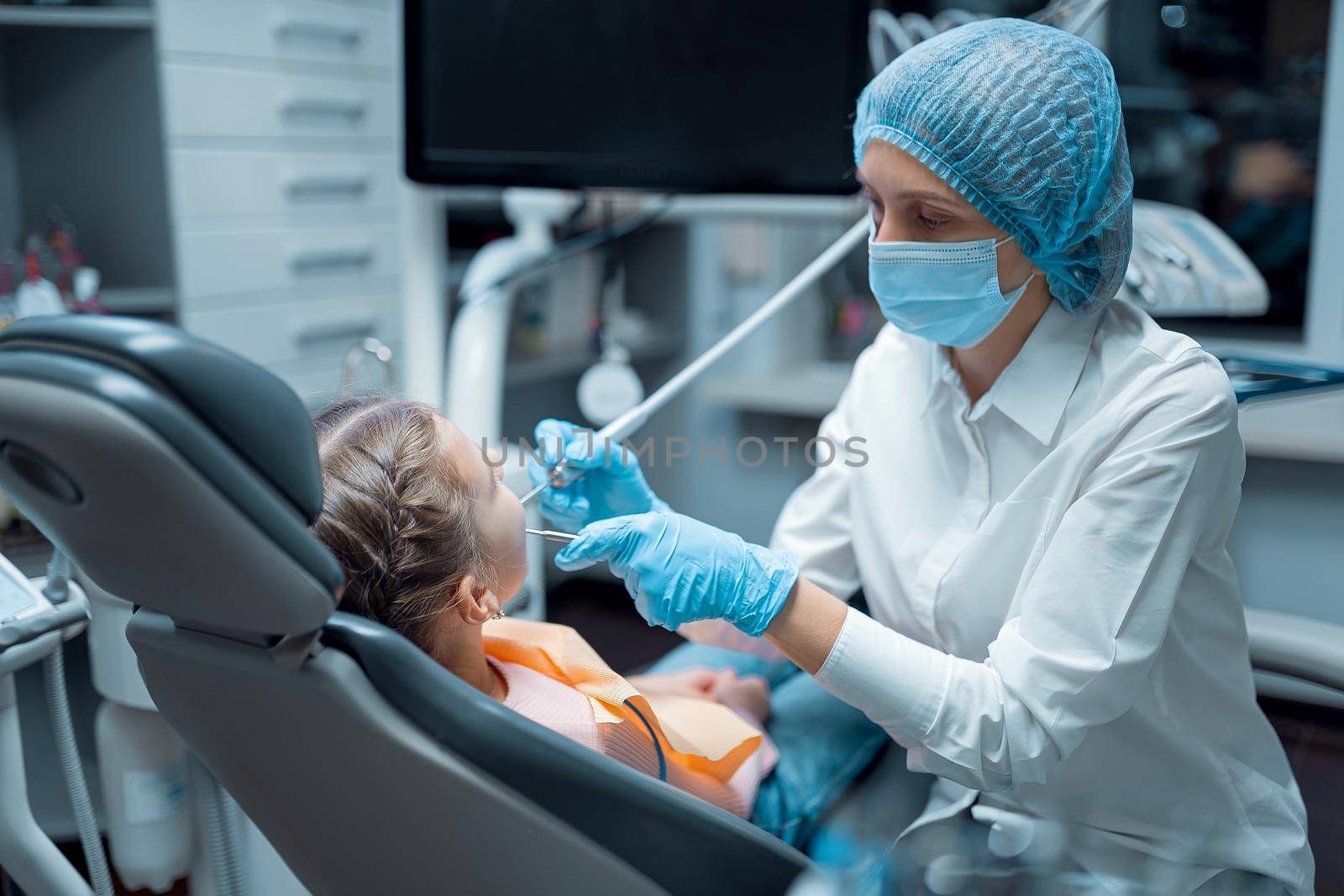Side view of Female dentist in medical uniform who treats teeth of little girl patient in dental office. Dentistry concept .