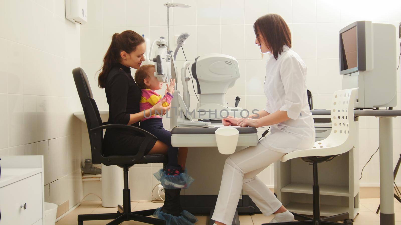Mother and daughter in the ophthalmologist's room- optometrist in clinic checking little child's vision, horizontal