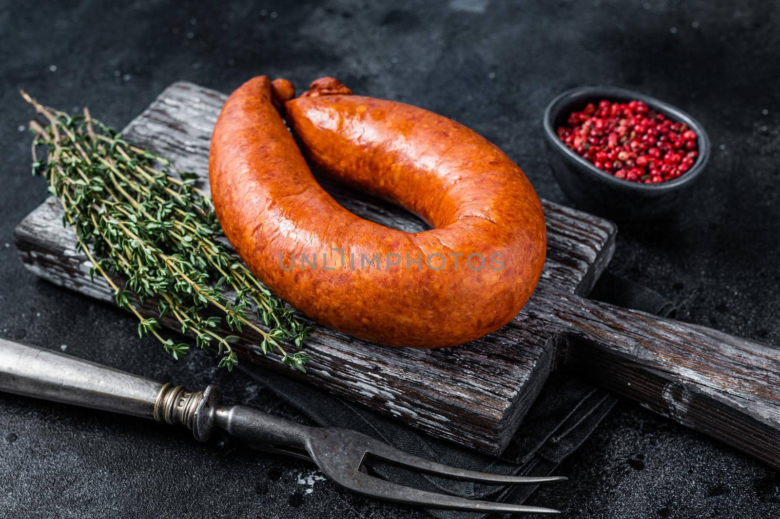 Bavarian Smoked sausage on a wooden rustic board with thyme. Black background. Top view.