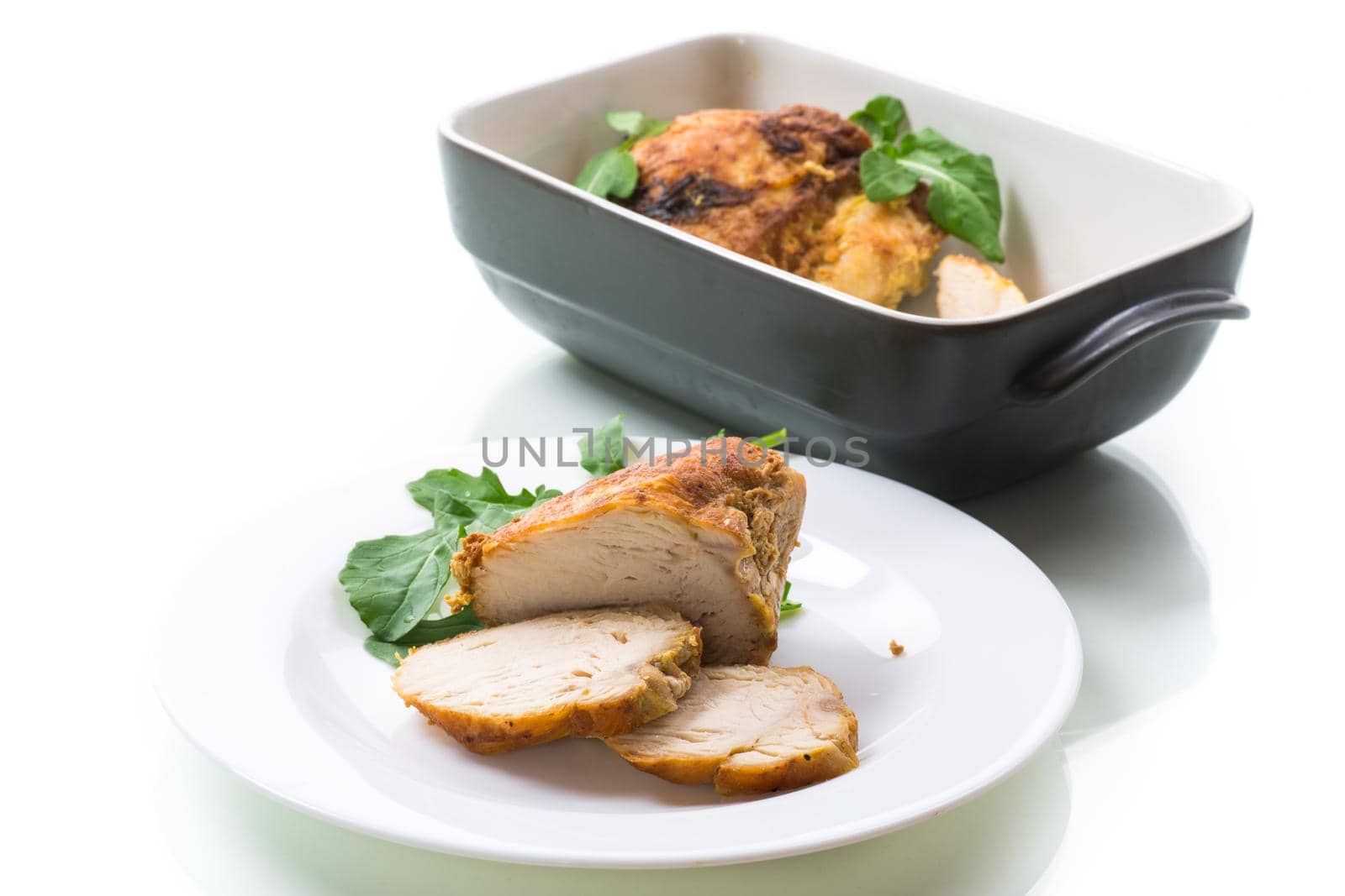 baked chicken fillet pieces with spices and herbs, in a plate on a white background