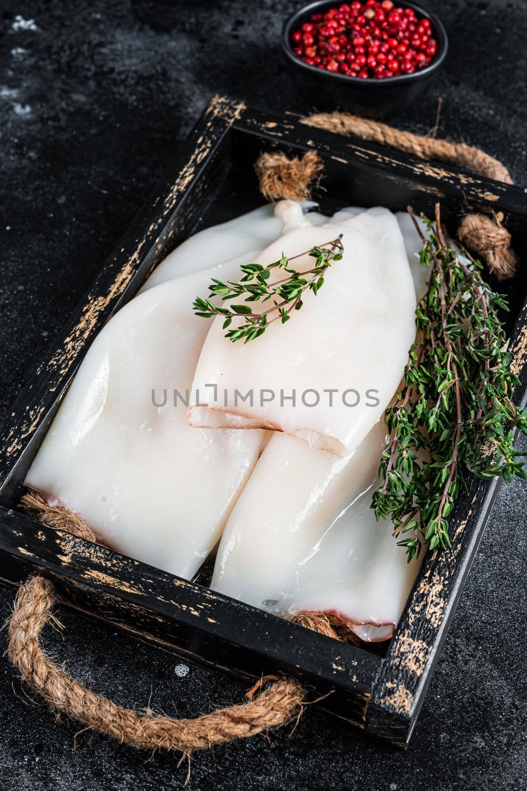 Raw white Squid or Calamari in a wooden tray with herbs. Black background. Top view by Composter