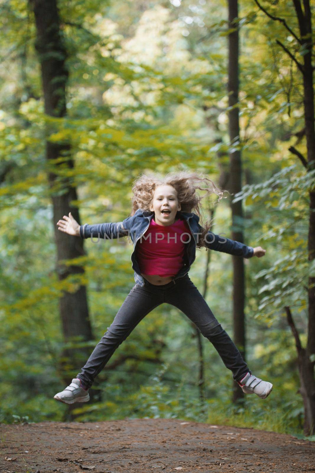 Little smiling girl child wearing jeans jacket - is jumping in park, outdoor portrait