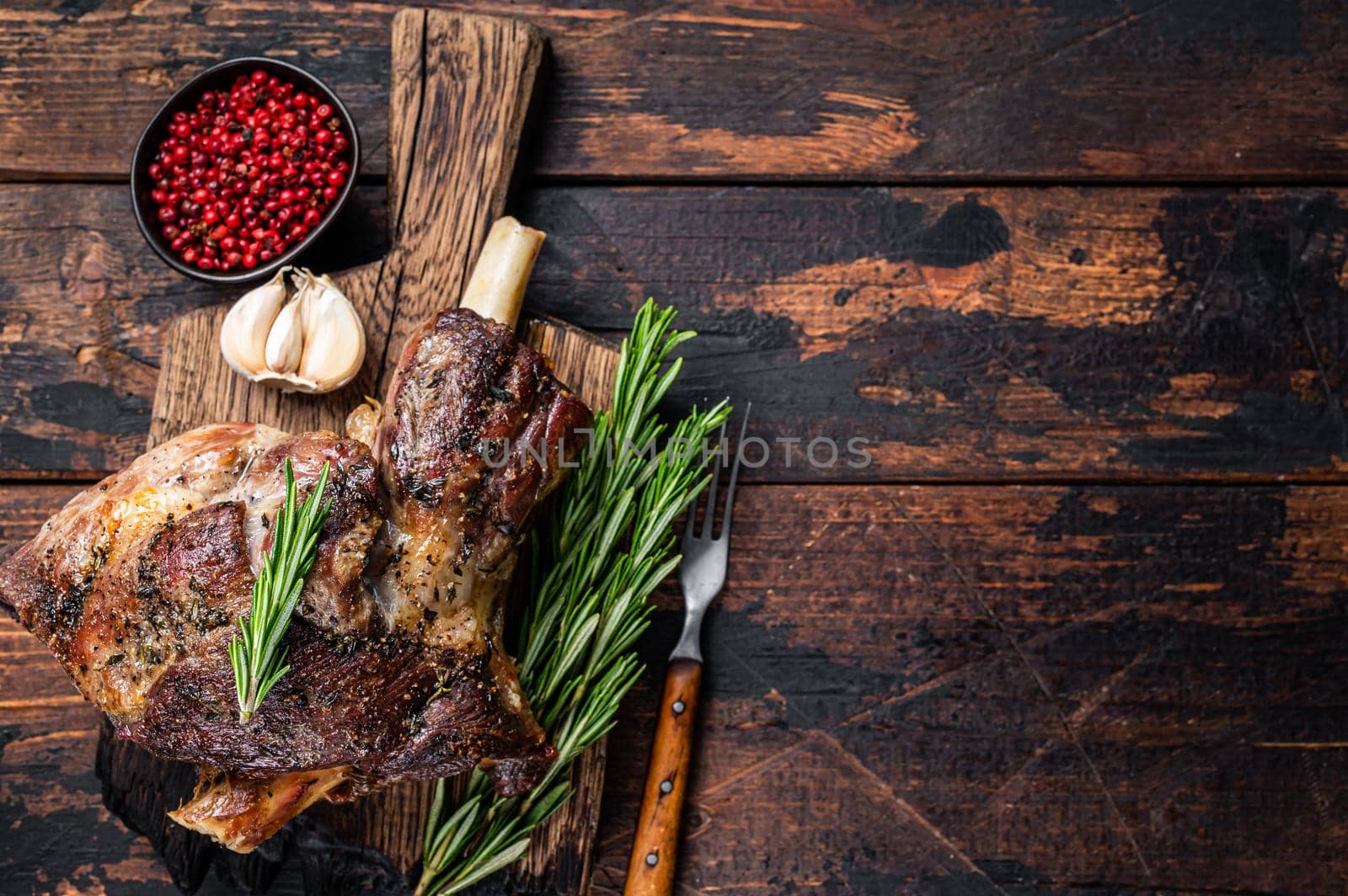 Baked lamb mutton leg meat on a wooden cutting board. Dark wooden background. Top view. Copy space by Composter