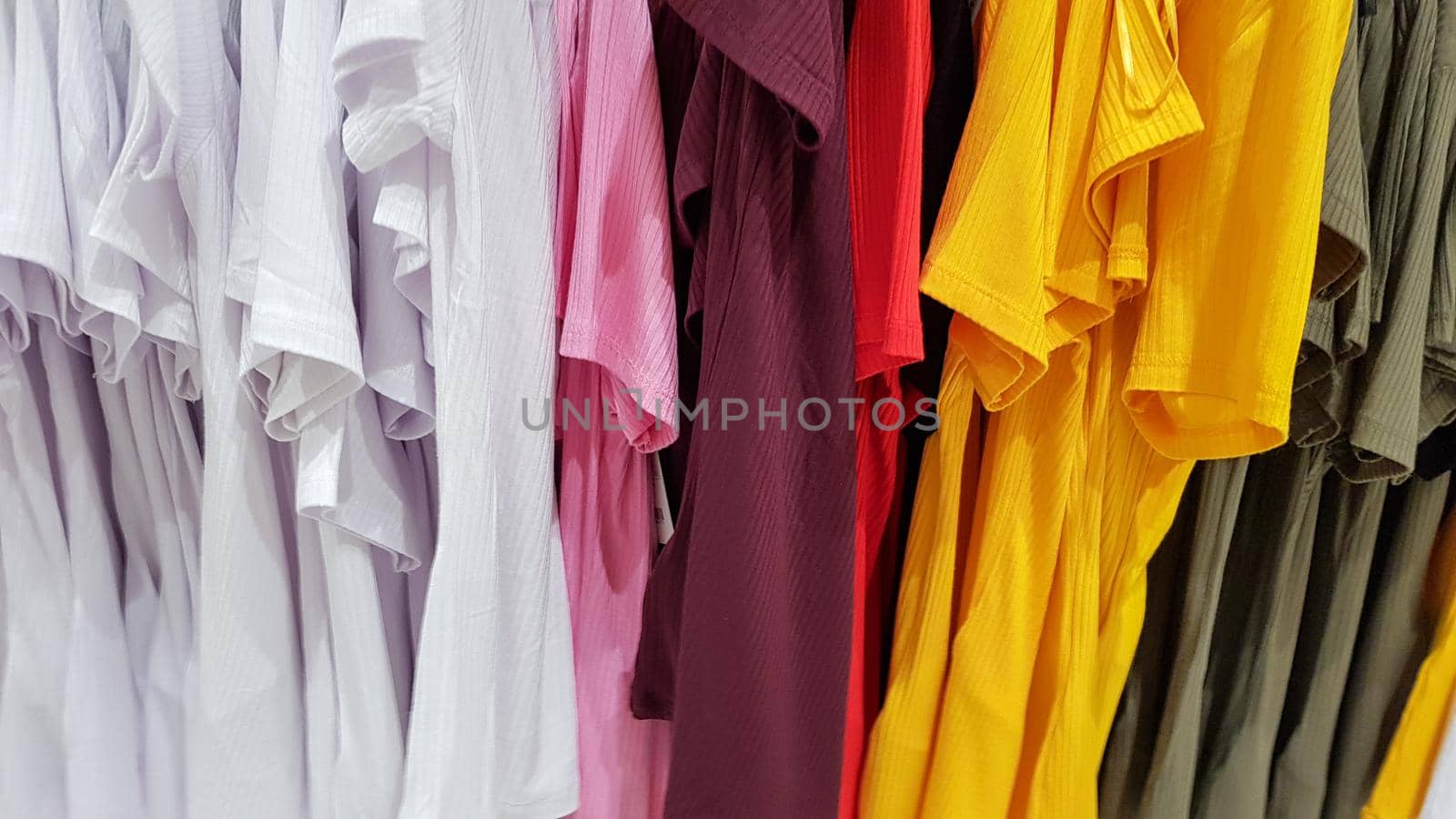 Colors of rainbow. Variety of casual shirts, t-shirts on hangers in a store. Cloth cotton of various bright colors close-up. Textile background.