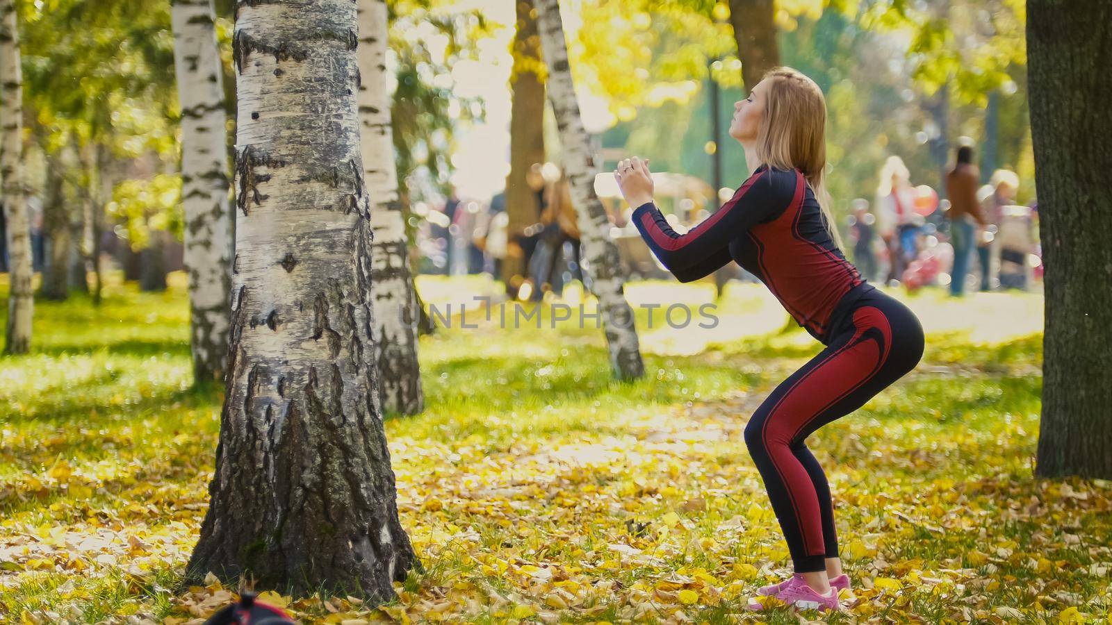 Sexy Attractive female blonde bikini-fitness model stretching in the autumn park on ground covered yellow leaves - sports squats, telephoto