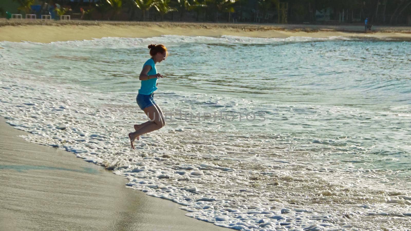 Young woman with long red hair play with waves running, feeling the sea, seascape beach of Dominican Republic, wide angle, Caribbean sea