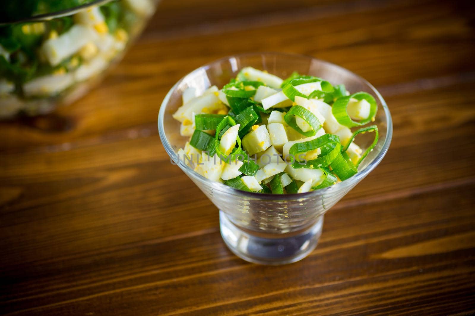 fresh spring salad with boiled squid, boiled eggs and green onions on a wooden table