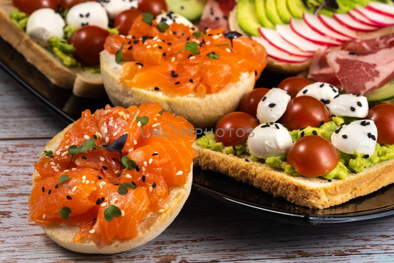 Assorted sandwiches with fish, cheese, meat and vegetables on a black plate.