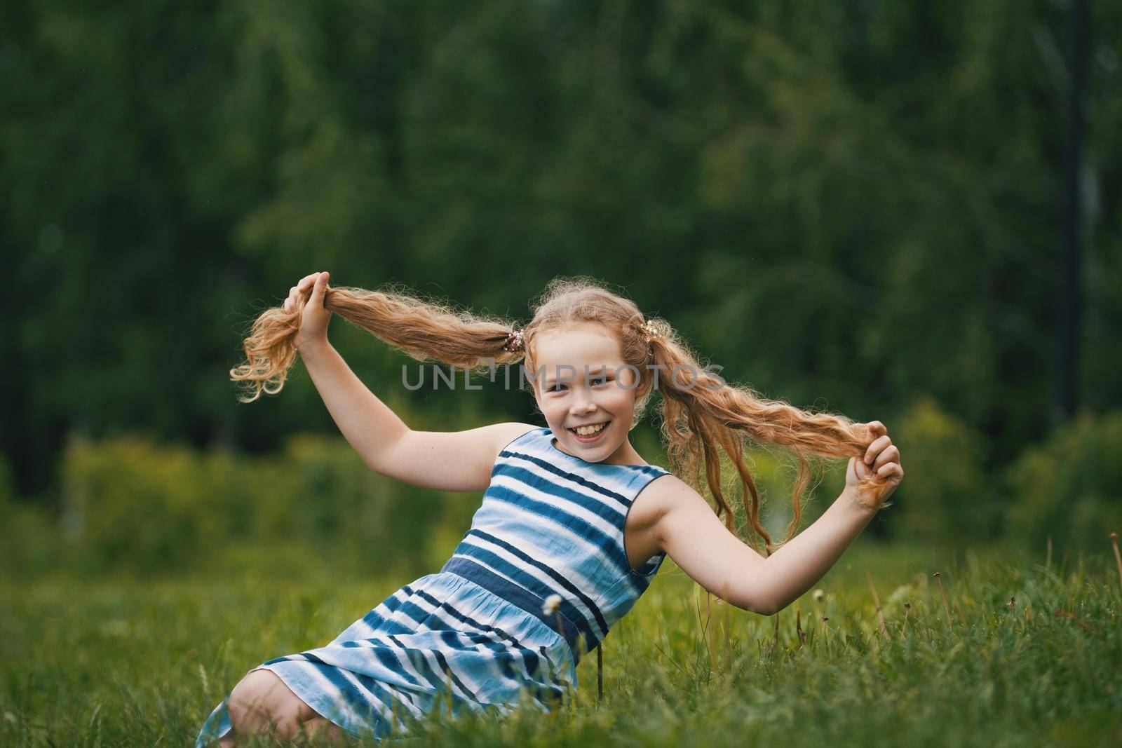 Smiling child girl wearing blue summer dress is playing in park, outdoor portrait