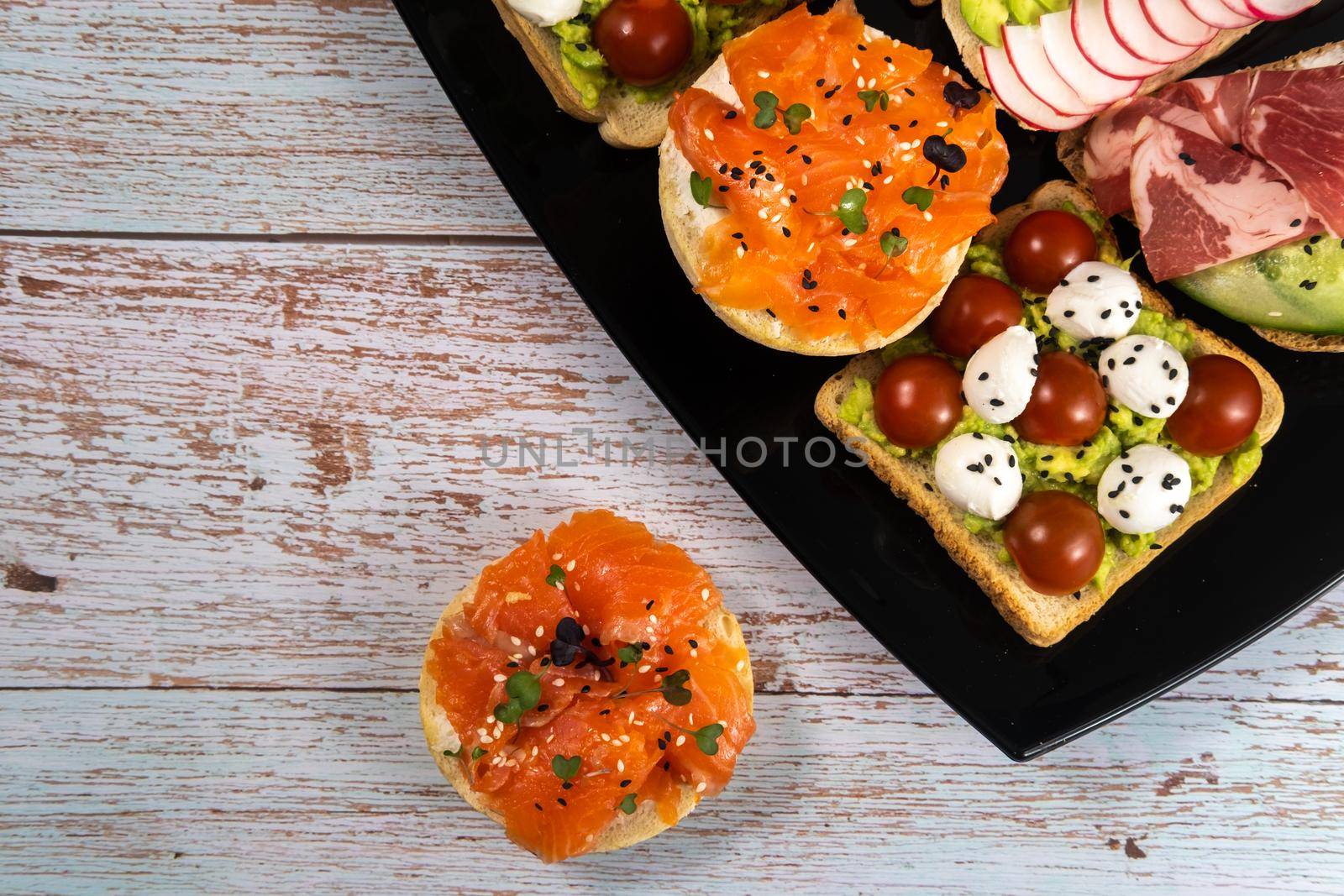 Assorted sandwiches with fish, cheese, meat and vegetables on a black plate.