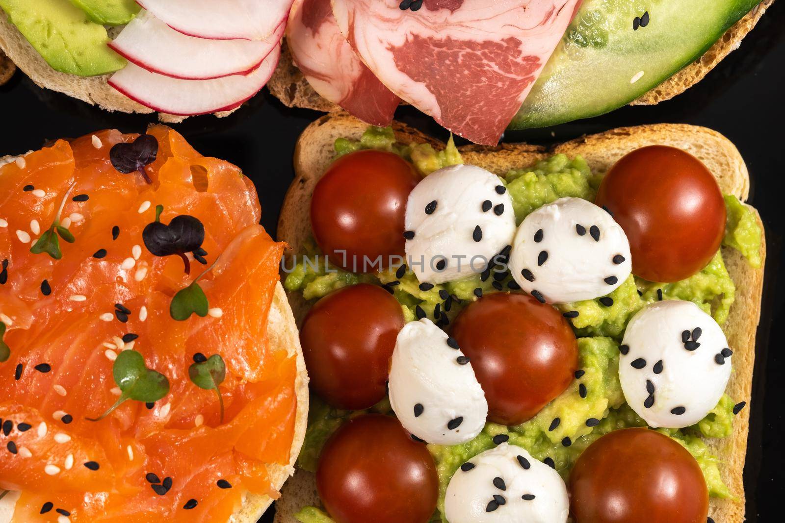 Assorted sandwiches with fish, cheese, meat and vegetables on a black plate.