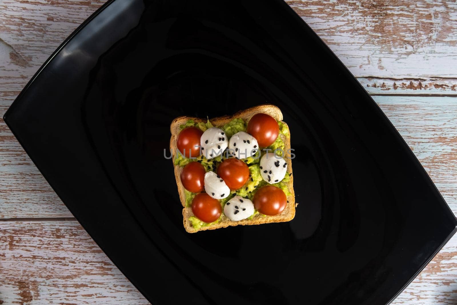 A cheese and tomato sandwich sits in a black plate on a wooden background.