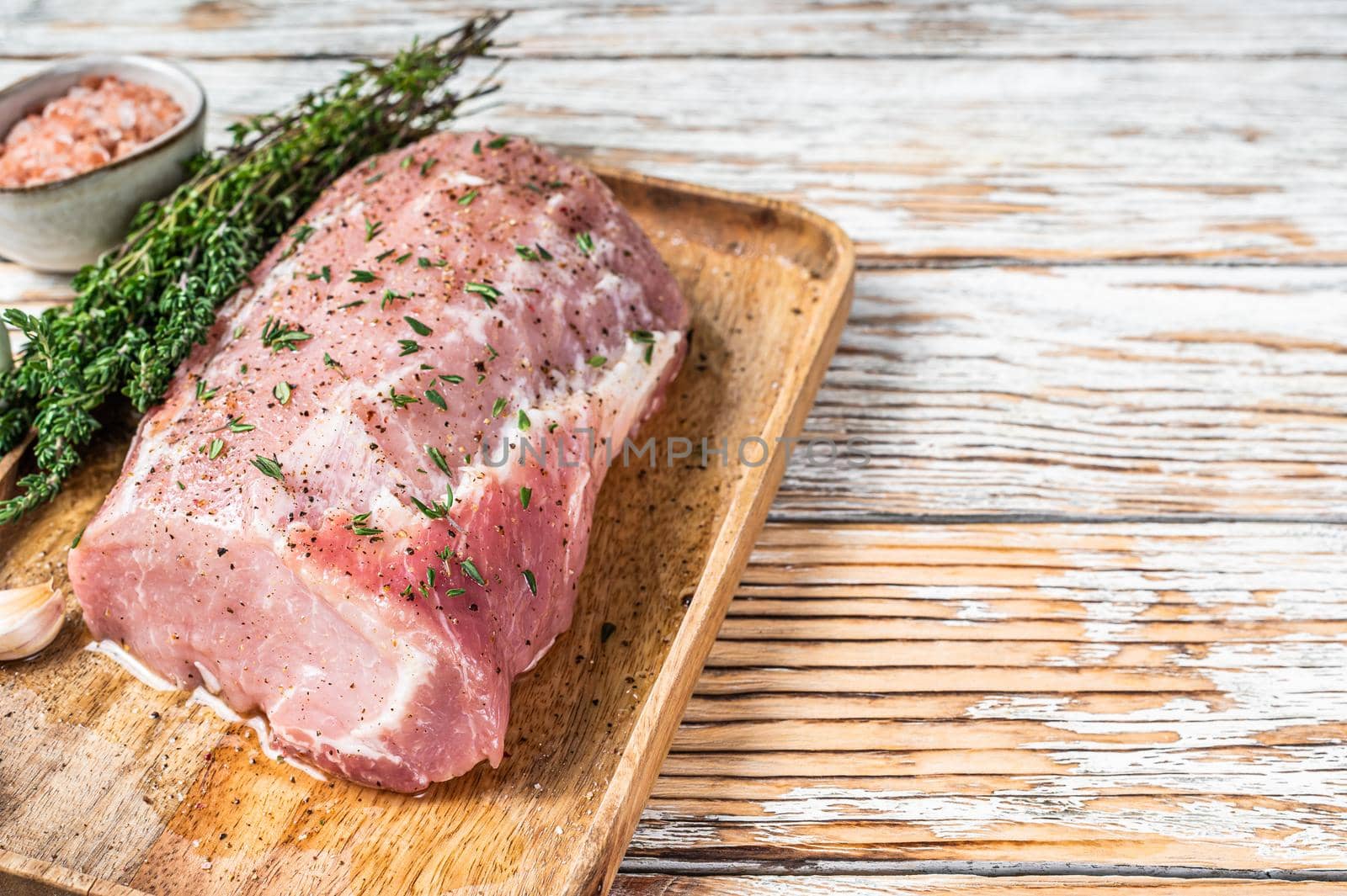 Raw Whole boneless pork loin meat with thyme and salt on rustic board. White wooden background. Top view. Copy space.