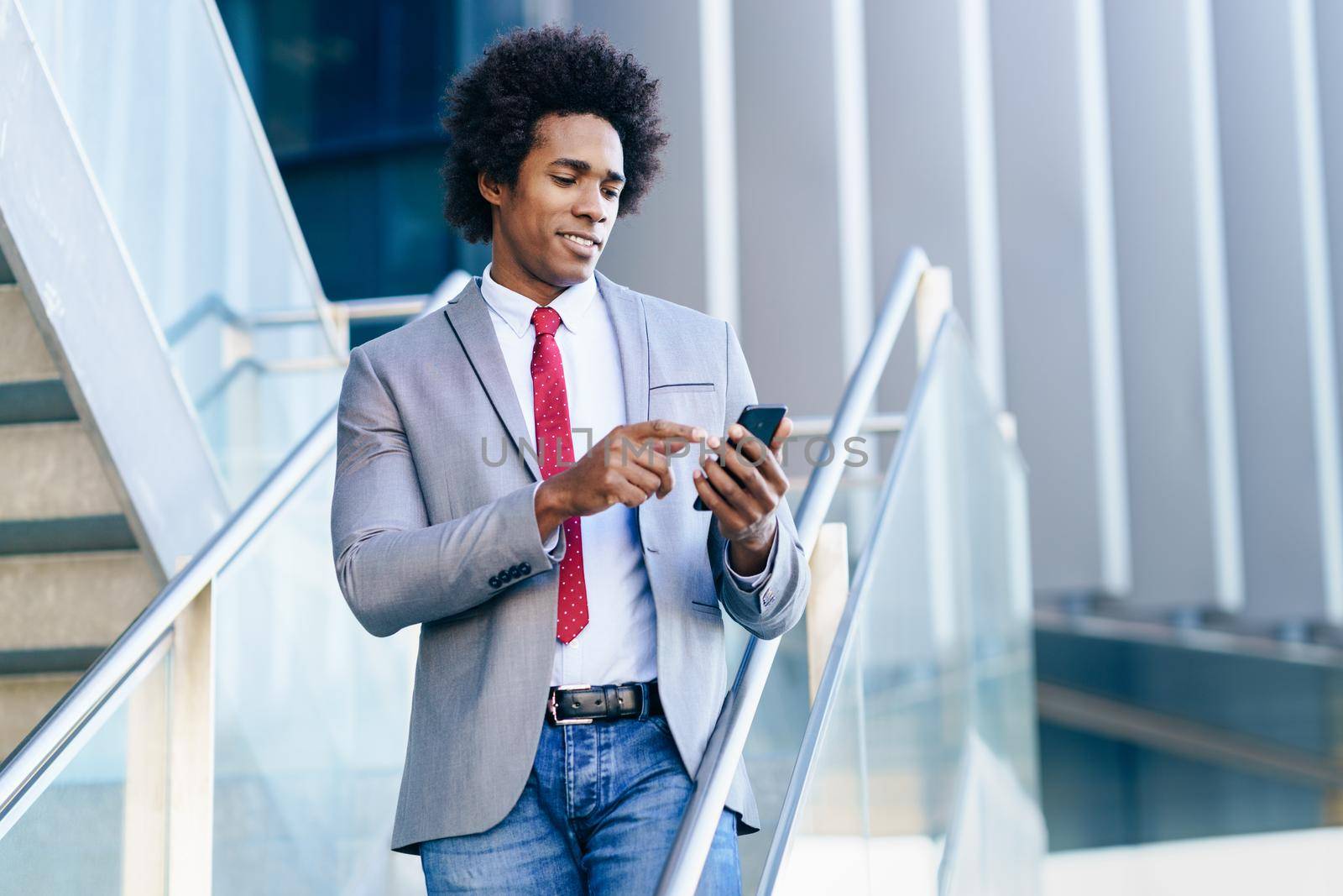 Black Businessman using his smartphone near an office building. Man with afro hair.