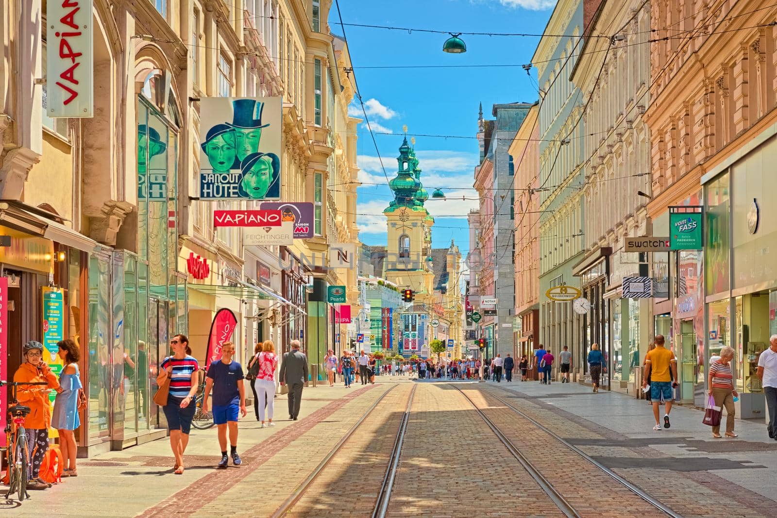 Linz - June 2020, Austria: View through the main street of the city with walking people, shops, and tram lines