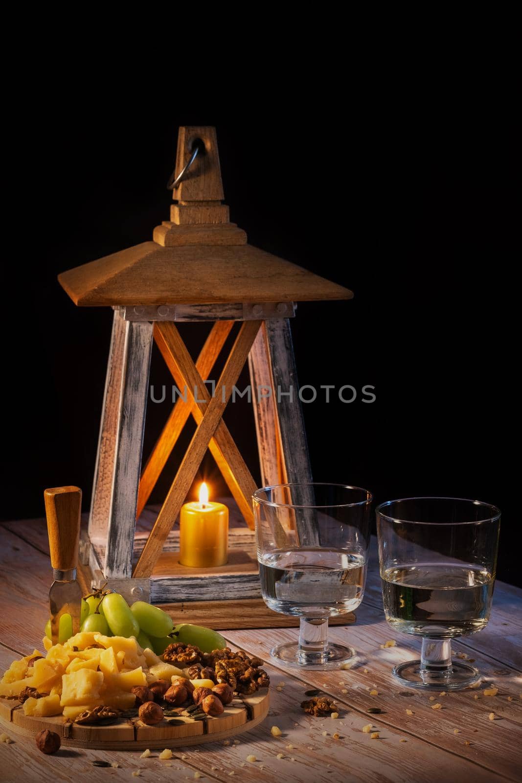 Cheese plate with a variety of snacks on the table with two glasses of wine by candlelight by Lobachad