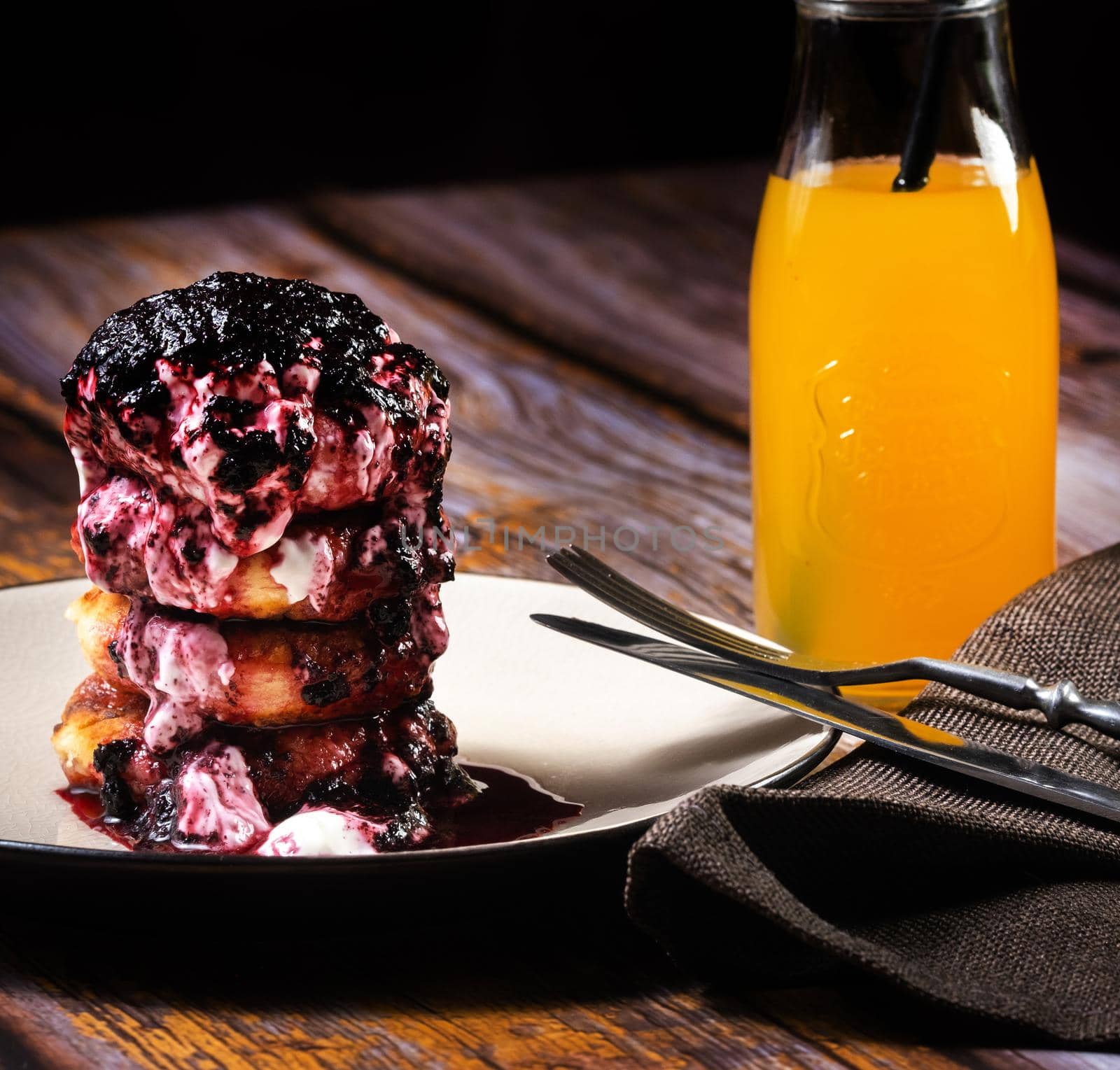 Fried Cheesecakes with blueberry jam and sour cream on a plate with orange juice in a bottle by Lobachad