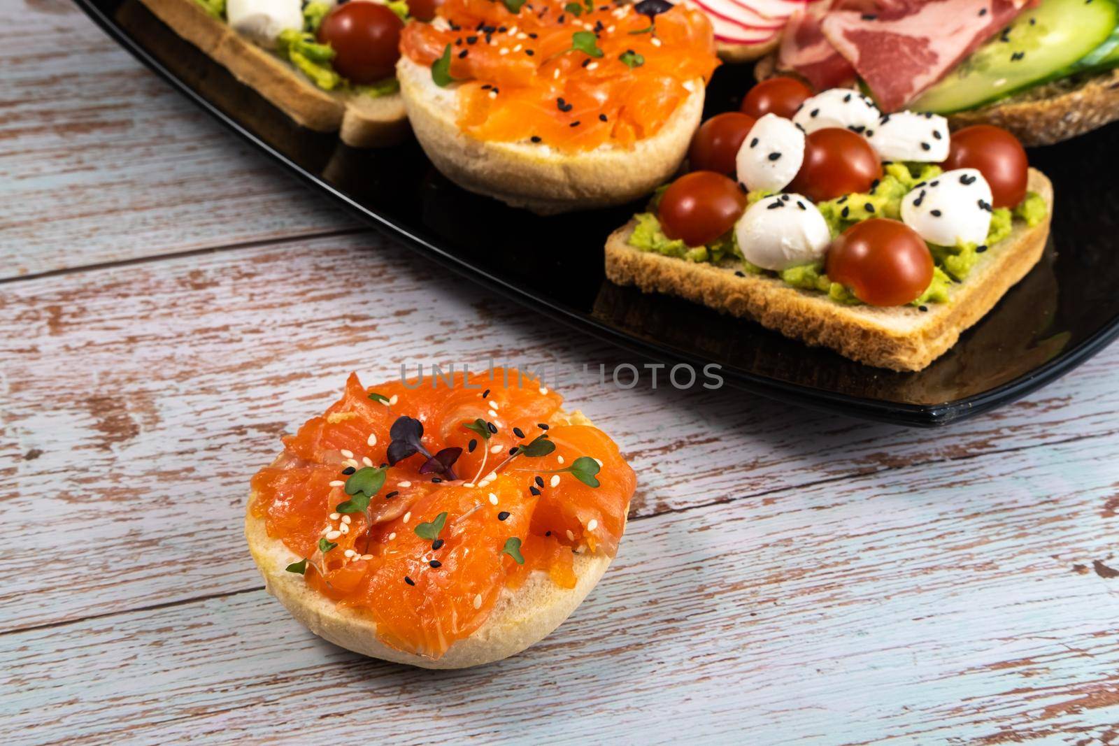 Assorted sandwiches with fish, cheese, meat and vegetables on a black plate by Lobachad
