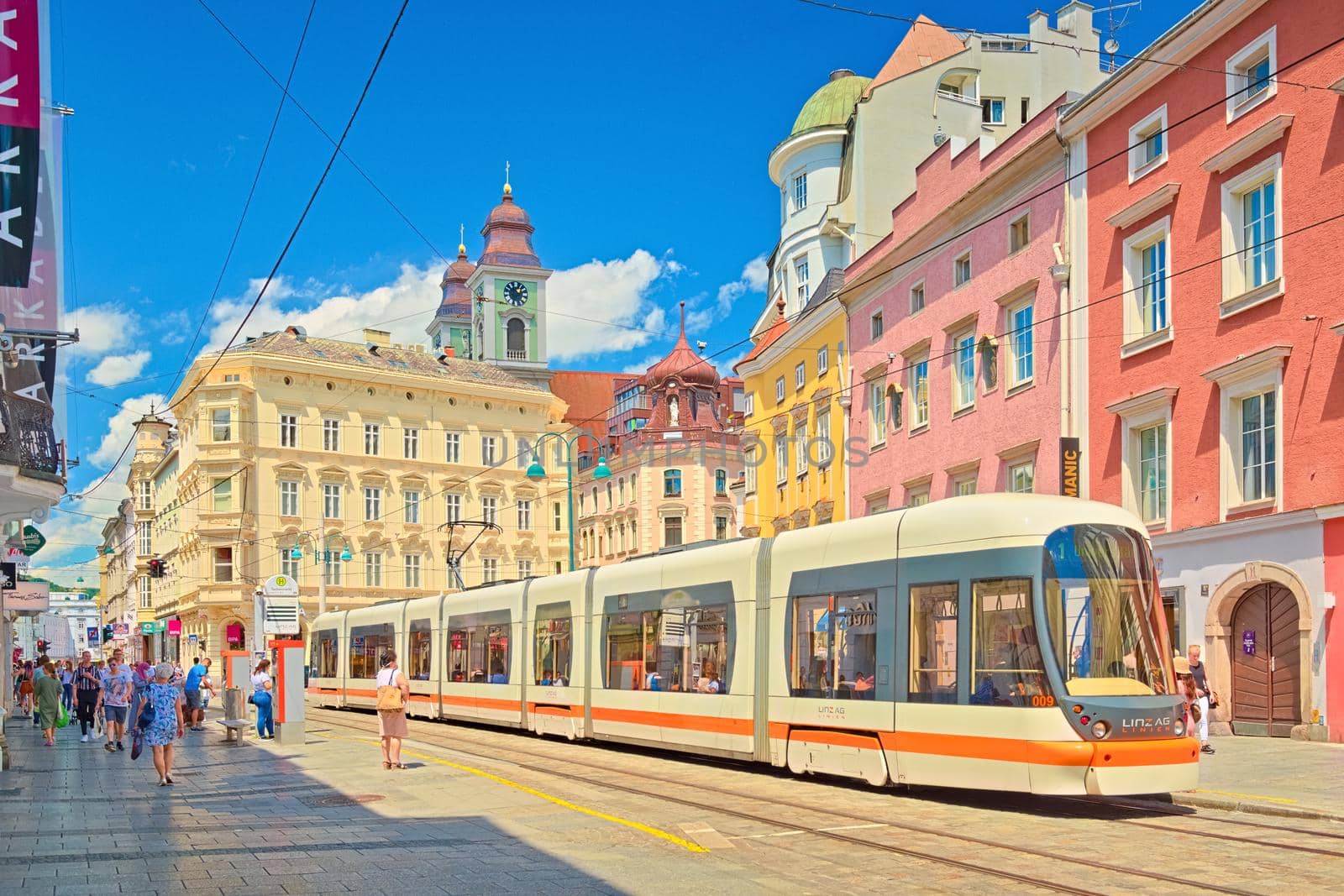 Linz - June 2020, Austria: View of the main street with walking people, a modern tram, and old colorful historical buildings