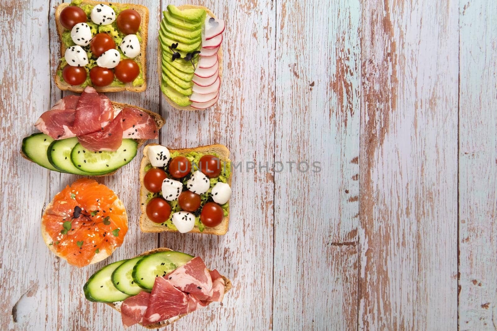 An assortment of sandwiches with fish, cheese, meat and vegetables lay on the wooden table by Lobachad